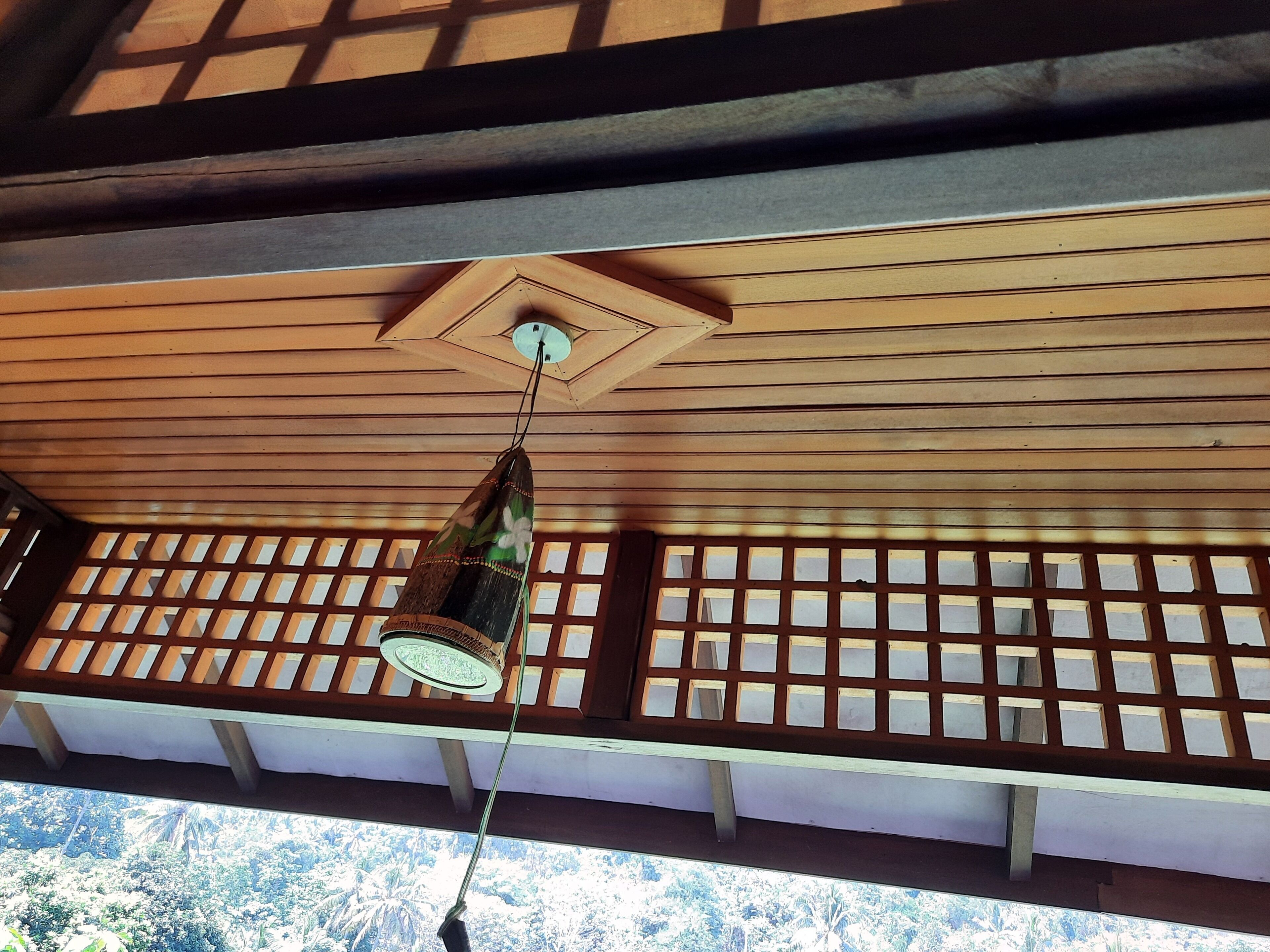 A traditional wooden ceiling with a hanging light fixture and a view of the outdoors through a lattice window.