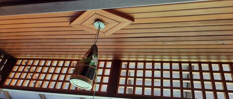 A traditional wooden ceiling with a hanging light fixture and a view of the outdoors through a lattice window.