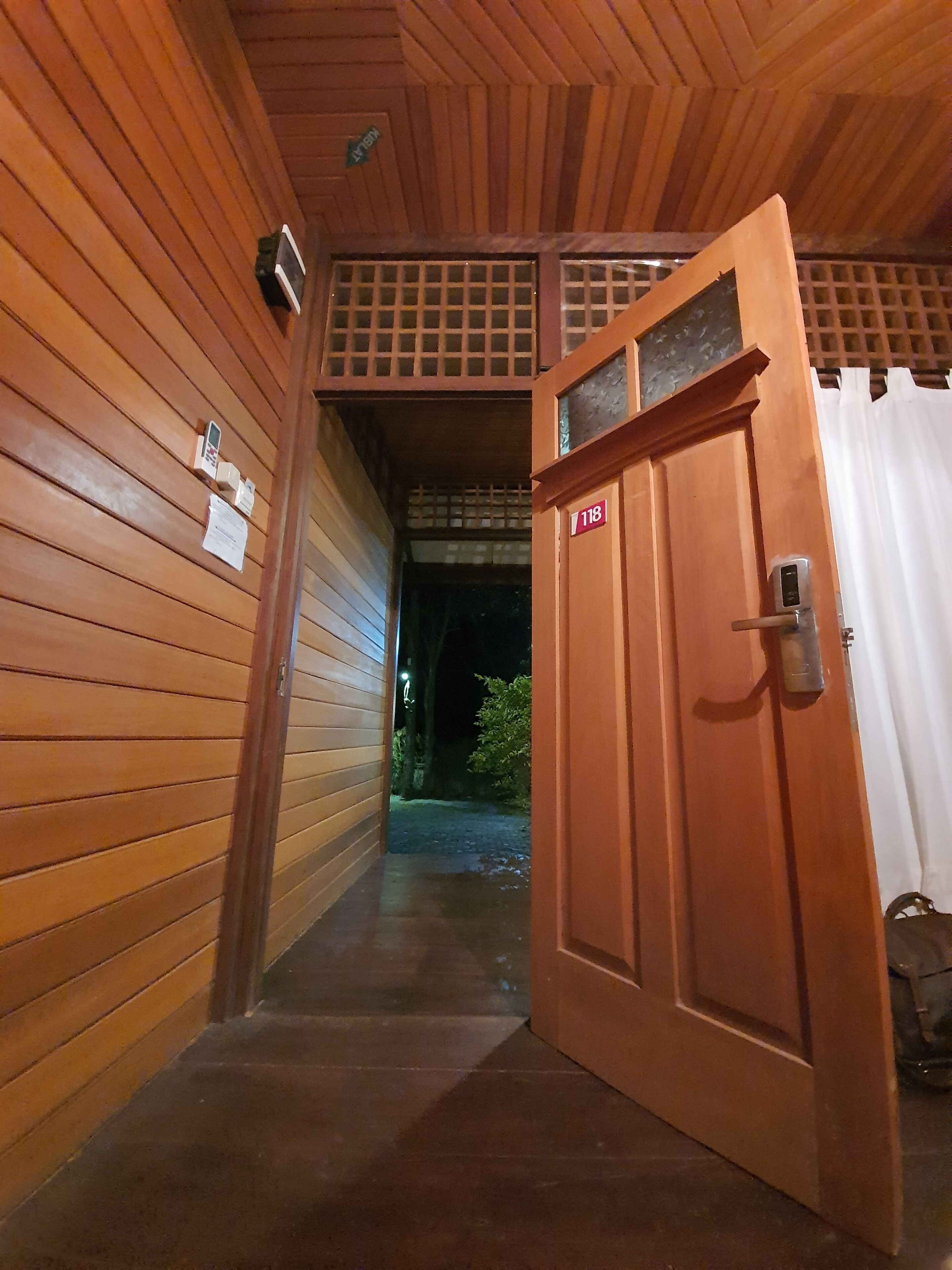 Un pasillo de madera con una puerta marcada '118' que da a un espacio exterior cubierto.