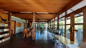 A spacious indoor area with wooden floors and high ceilings, featuring a long table with a buffet setup and a bookshelf filled with books. - Hotel Besar Bulan Baru - Senggigi (Senggigi)