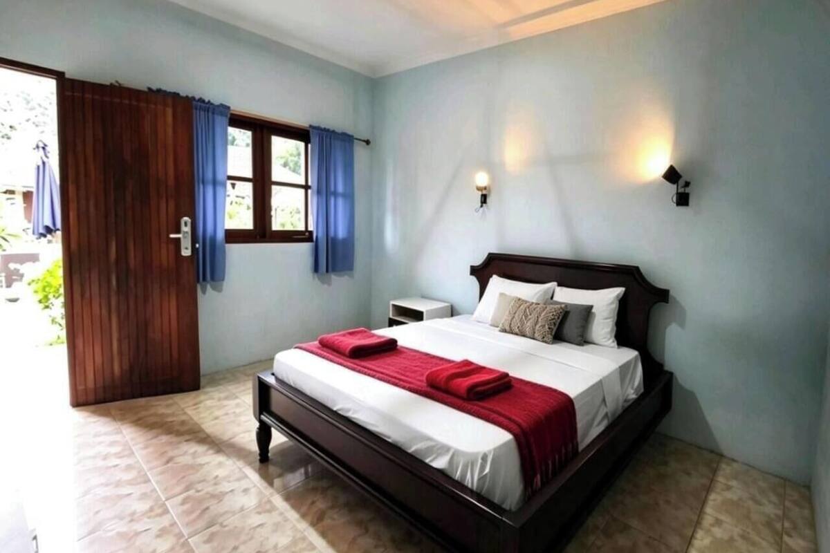 A bedroom with a bed, a nightstand, a window with curtains, and a door.