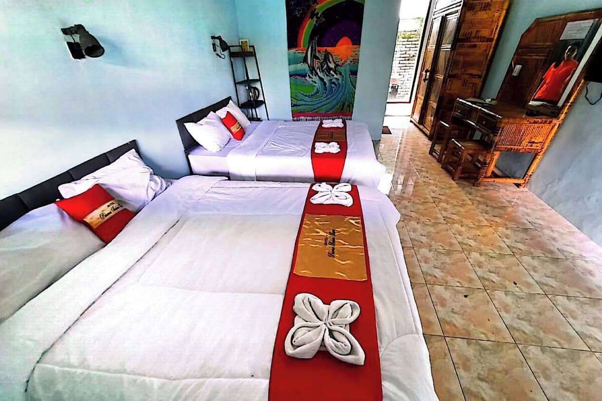 A hotel room with two beds, each with white linens and red decorative pillows.