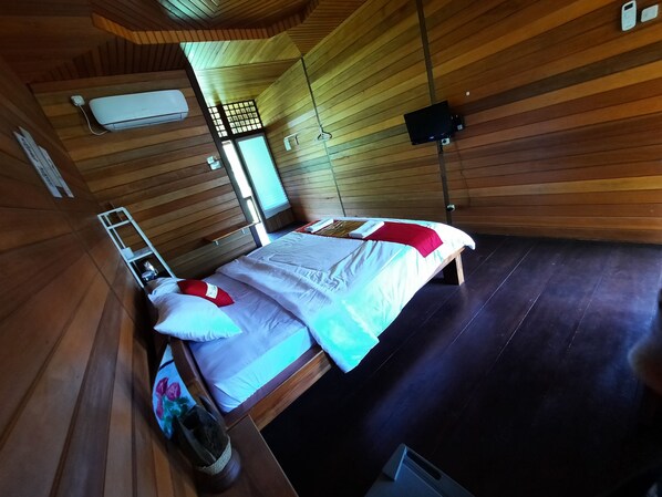 A wooden room with a bed, a ladder, a small table, and a wall-mounted TV. - Hotel Besar Bulan Baru - Senggigi (Senggigi)