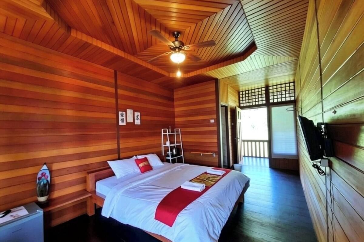A wooden-paneled room with a bed, a nightstand, a TV, and a ceiling fan.