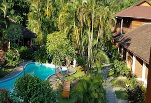 Une piscine entourée d’une végétation luxuriante et un bâtiment en bois doté d’un toit en tuiles.