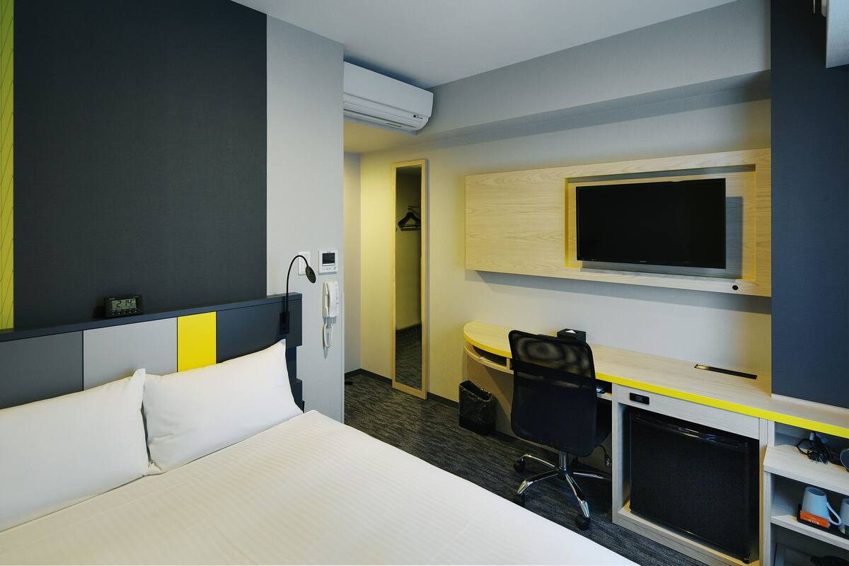 Ein Hotelzimmer mit einem Bett, einem Schreibtisch mit Computer, einem Fernseher und einem Kleiderschrank.