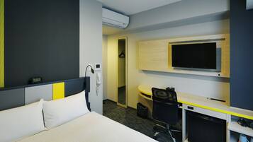 Una habitación de hotel con una cama, un escritorio con computadora, un televisor y un armario.
