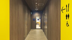 A hallway with wooden walls and a yellow accent wall, leading to a room with a sign indicating a men's and women's restroom and a wheelchair-accessible facility.