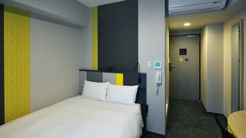 A hotel room with a bed, a desk, and a chair. There is a phone on the wall and a door leading to another room.