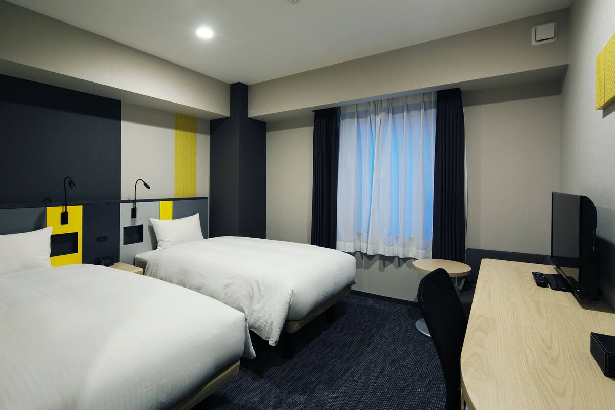 Ein Hotelzimmer mit zwei Betten, einem Schreibtisch, einem Stuhl und einem Fernseher.