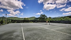 Un campo da tennis con una rete, circondato da vegetazione e colline.
