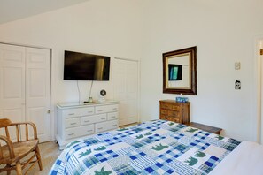 Un dormitorio con cama, cómoda, televisor, espejo y silla.