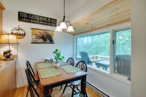 A dining area with a wooden table, chairs, a hanging light fixture, a wall sign, and a window with a view of the outdoors. - Steps to Sugar Mountain! Condo w/ Furnished Deck (Sugar Mountain)