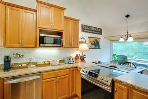 Una cocina con gabinetes de madera, microondas integrado, cafetera, tostadora y estufa.