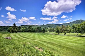 A well-maintained grassy field with trees and a mountain in the background. - Steps to Sugar Mountain! Condo w/ Furnished Deck (Sugar Mountain)