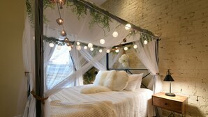Une chambre à coucher avec un lit à baldaquin, du linge de lit blanc, une table de chevet avec une lampe et un mur en briques.
