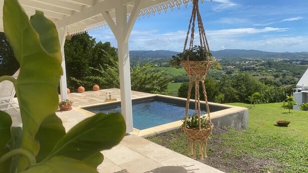 Zona de piscina con una pérgola, plantas en macetas y vistas al campo.