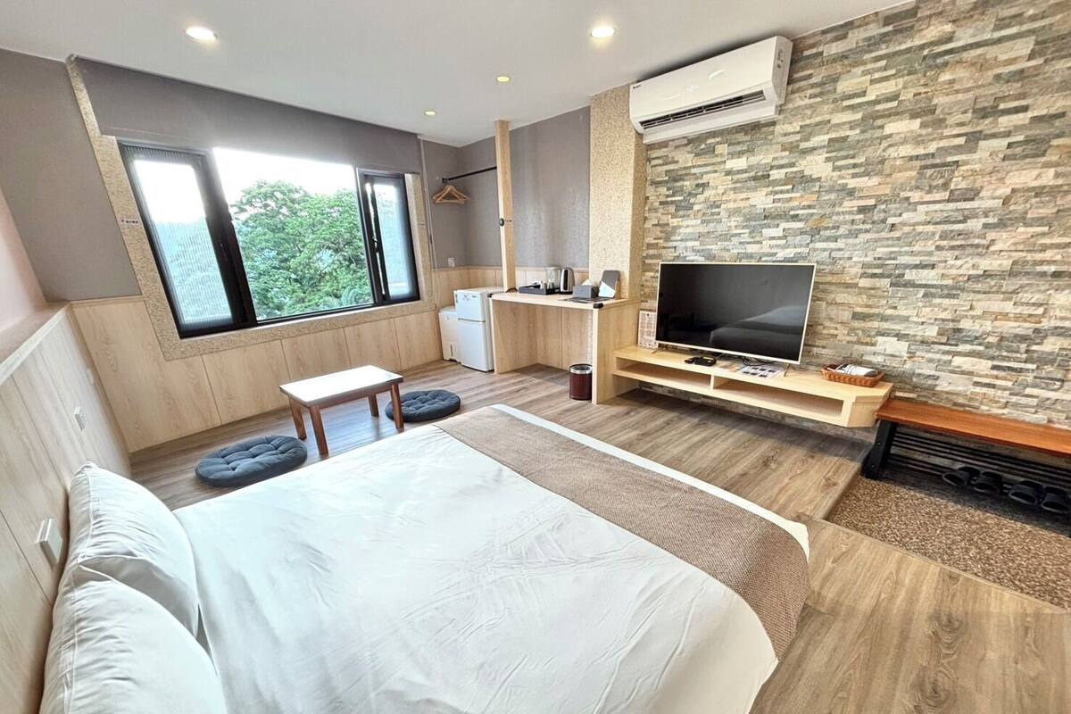 A modern bedroom with a large bed, a TV, a small desk, and a stone wall.