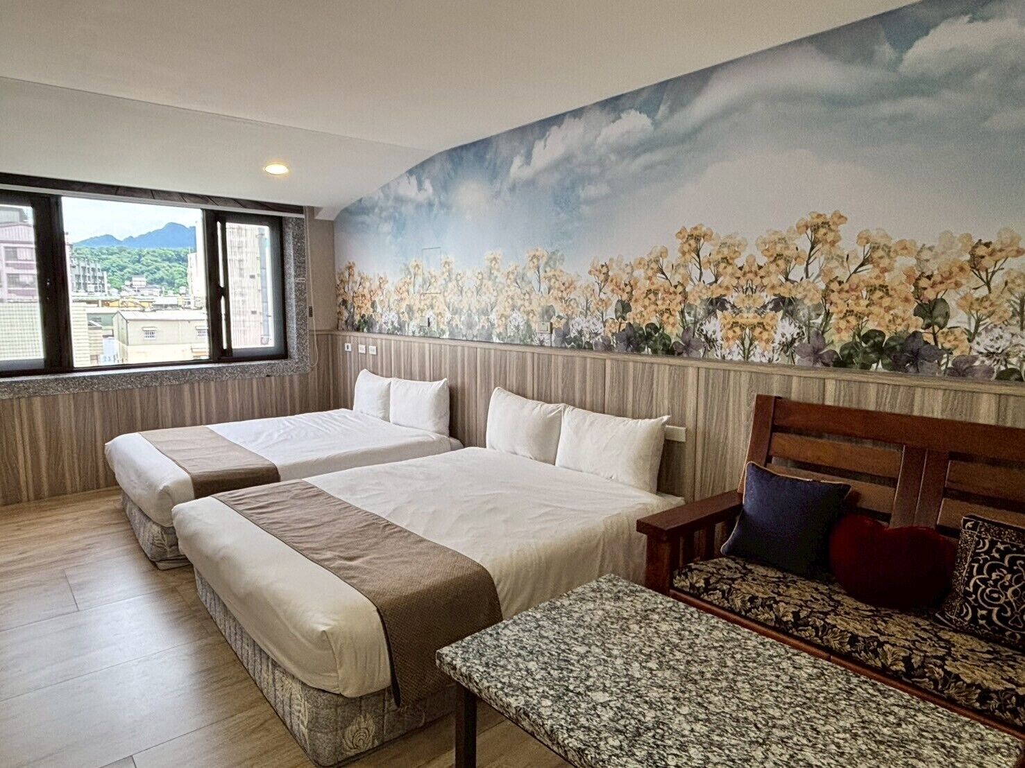 A hotel room with two beds, a bench, and a mural of flowers on the wall.
