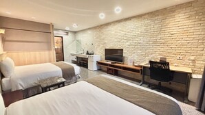 A hotel room with two beds, a TV, a desk, and a brick wall.