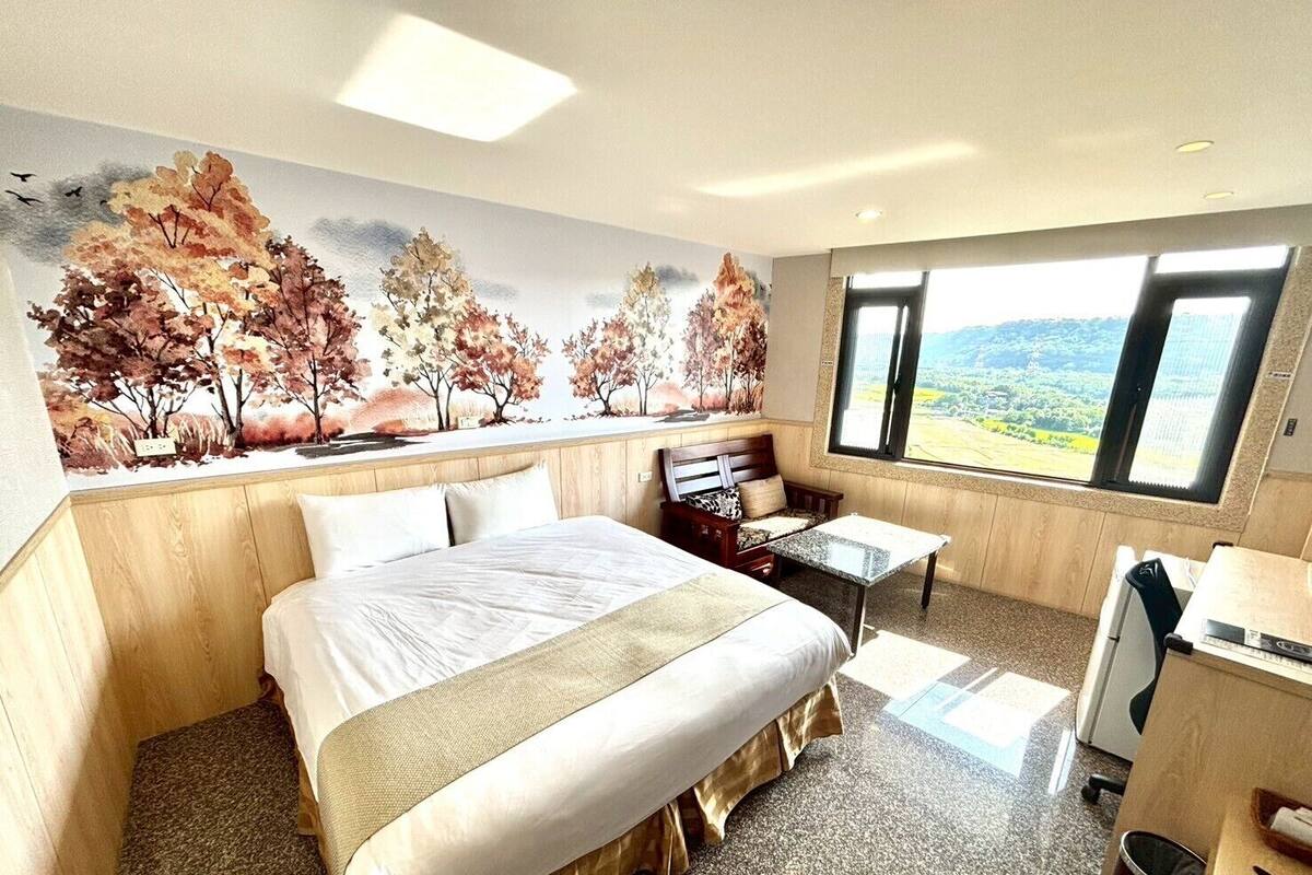 A hotel room with a large bed, a desk, and a view of the outdoors.