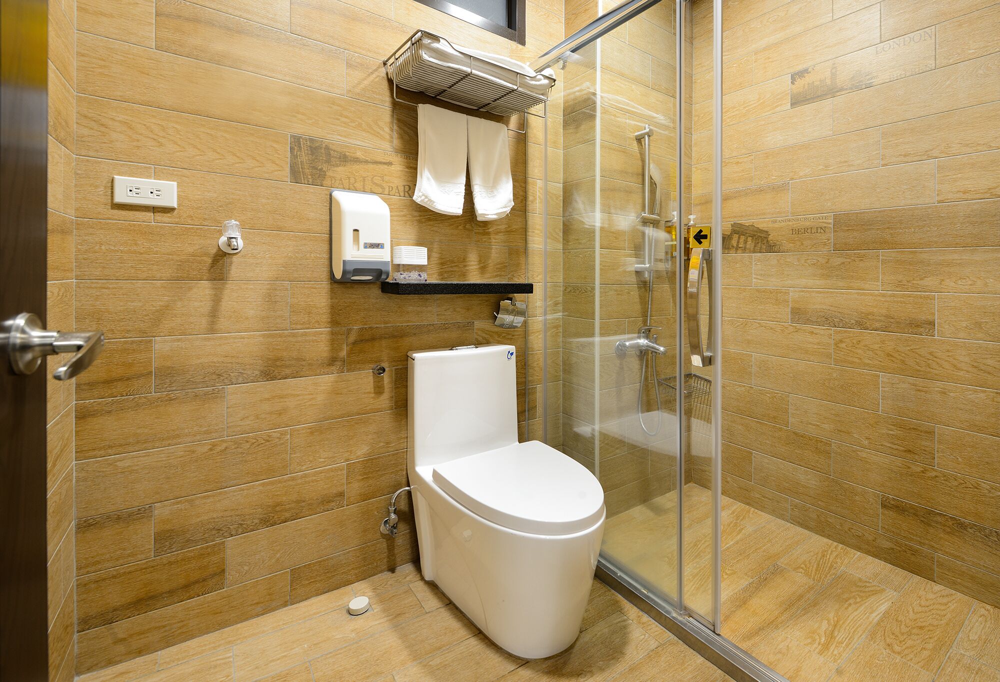 A bathroom with a toilet, a glass shower enclosure, and a towel rack with towels.
