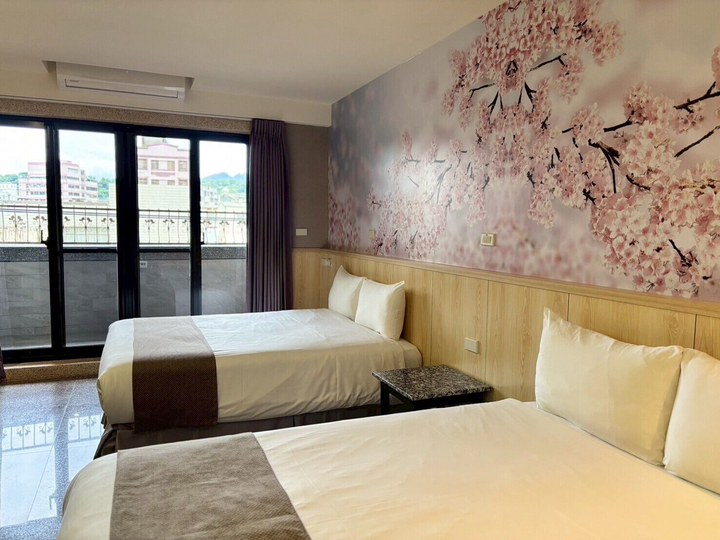 Ein Hotelzimmer mit zwei Betten, einem großen Fenster mit Ausblick und einer Kirschblüten-Wandmalerei.