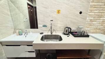 A modern bathroom with a marble floor, a sink with a faucet, a mirror, and a coffee maker.