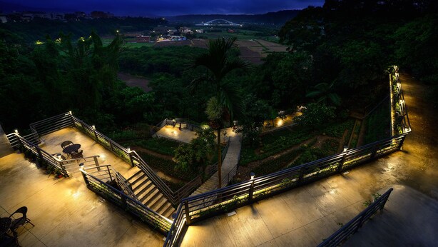 A well-lit outdoor area with a staircase, seating, and a view of a bridge in the distance.