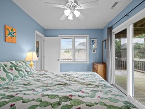 Un dormitorio con cama, ventilador de techo, ventana, puerta y vista a una terraza.