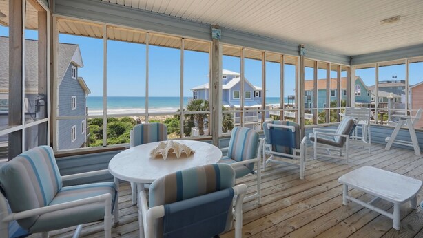 Un espace extérieur abrité, avec vue sur la plage, comprenant des chaises à rayures, une table et une petite table blanche.