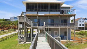 Une maison de deux étages située en bord de mer, dotée d’un balcon, d’une terrasse en bois et offrant une vue dégagée sur l’océan.