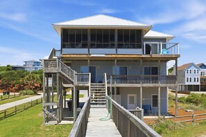 Uma casa à beira-mar de dois andares, com varanda, deck de madeira e vista desobstruída para o oceano.