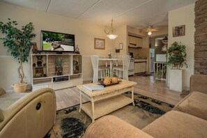 Ein Wohnzimmer mit Fernseher, einer Sitzecke und einer Küche im Hintergrund.