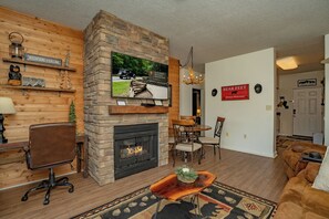 Ein Wohnzimmer mit Kamin aus Stein, Holzwänden, einem an den Kamin montierten Fernseher und einem Schild mit der Aufschrift 'Great Smoky Mountains National Park'.