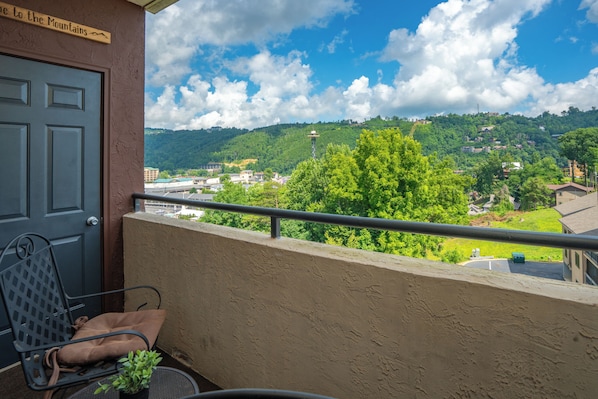 Ein Balkon mit Stuhl und Topfpflanze, mit Blick auf eine Stadt, die Gebäude und Hügel zeigt.