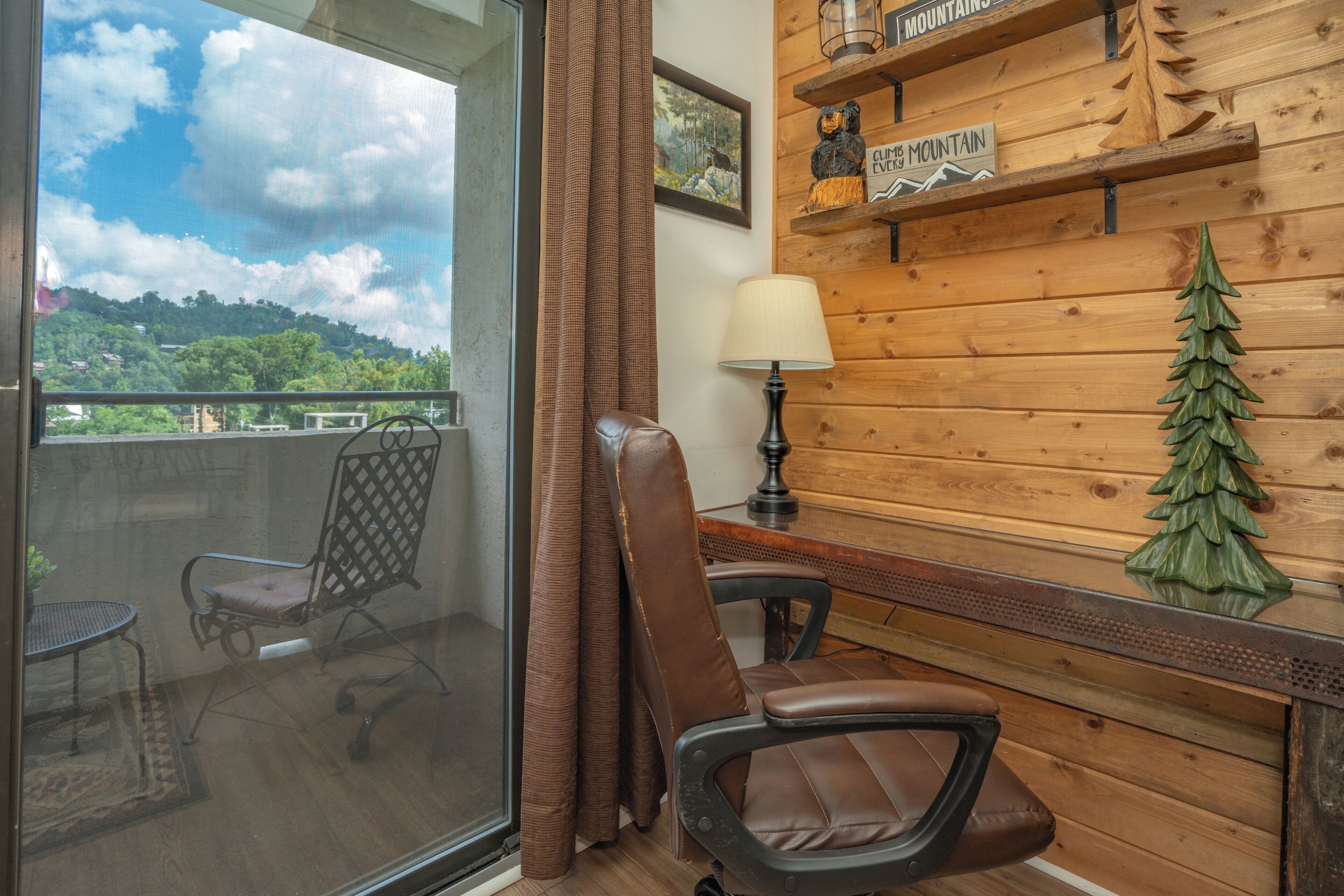 A room with a balcony, a chair, a table, a lamp, and a wooden wall with a sign.
