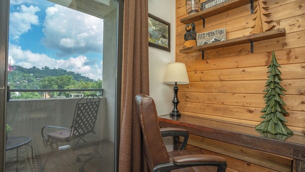 Una habitación con balcón, una silla, una mesa, una lámpara y una pared de madera con un cartel.