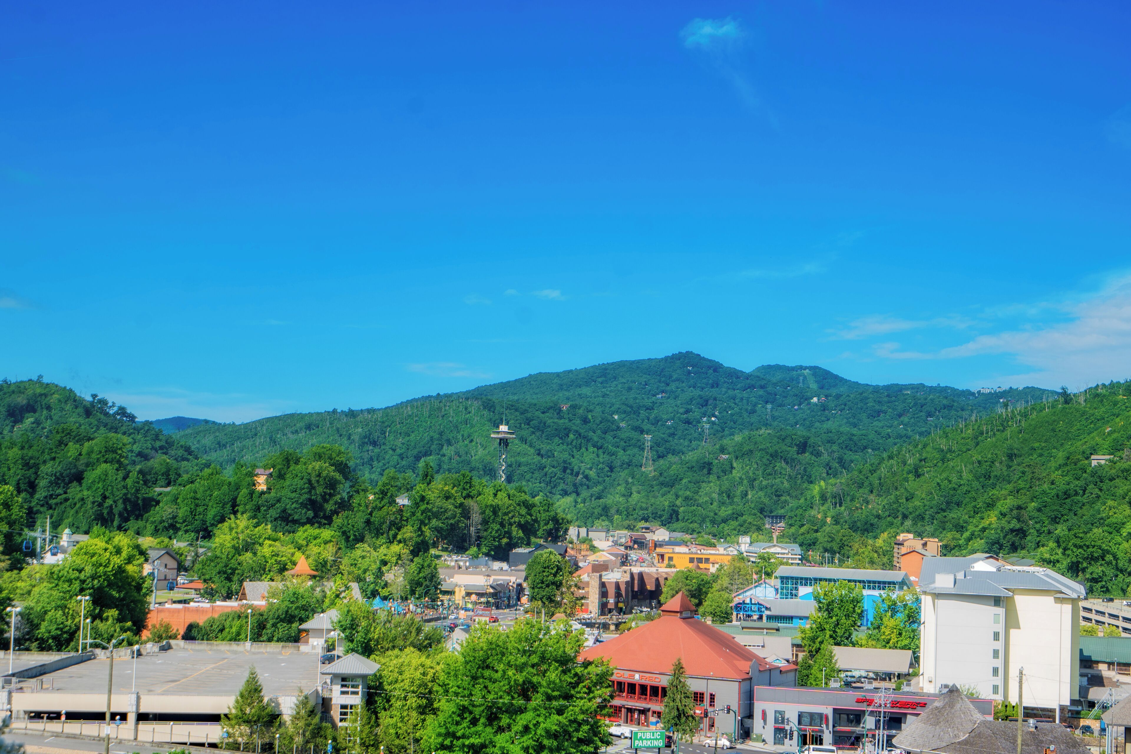 A town with a mix of commercial and residential buildings, a clear blue sky, and a hilly backdrop.