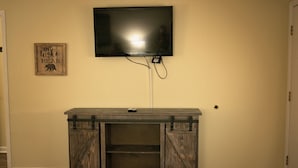 Un salón con televisor de pantalla plana montado, un mueble de madera para equipos electrónicos y una cita enmarcada en la pared.