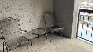 Un balcón con pared texturizada, una silla de metal y una pequeña mesa redonda.