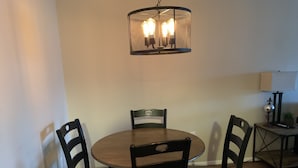 Un comedor con una mesa redonda de madera y cuatro sillas. Un lámpara colgante con tres bombillas ilumina la mesa.