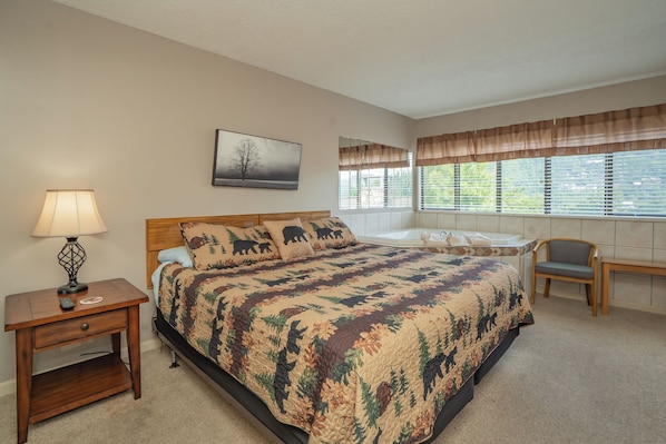 A bedroom with a bed, bedside table, lamp, and a window with blinds.
