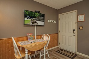A dining area with a wooden table and chairs, a television mounted on the wall, and a door with a coat hook.