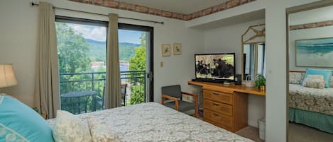 Habitación de hotel con cama, escritorio con computadora, silla, ventana con vista a la vegetación y balcón.