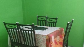 A dining area with a green wall, a table covered with a patterned tablecloth, and four chairs. - Village No Thrill 2 Bed (Gros Islet)