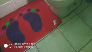 A bathroom with a toilet, a green wall, a pink shower curtain, and a red mat with footprints. - Village No Thrill 2 Bed (Gros Islet)