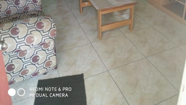 A living room with a sofa, a small table, a television on a cabinet, and a patterned chair. - Village No Thrill 2 Bed (Gros Islet)
