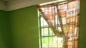 A small, green-walled room with a single bed, a window with patterned curtains, and a tiled floor. - Village No Thrill 2 Bed (Gros Islet)
