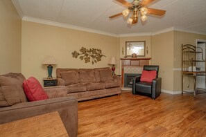 A living room with a brown sofa, a black leather chair, a wooden coffee table, a ceiling fan, and a fireplace.